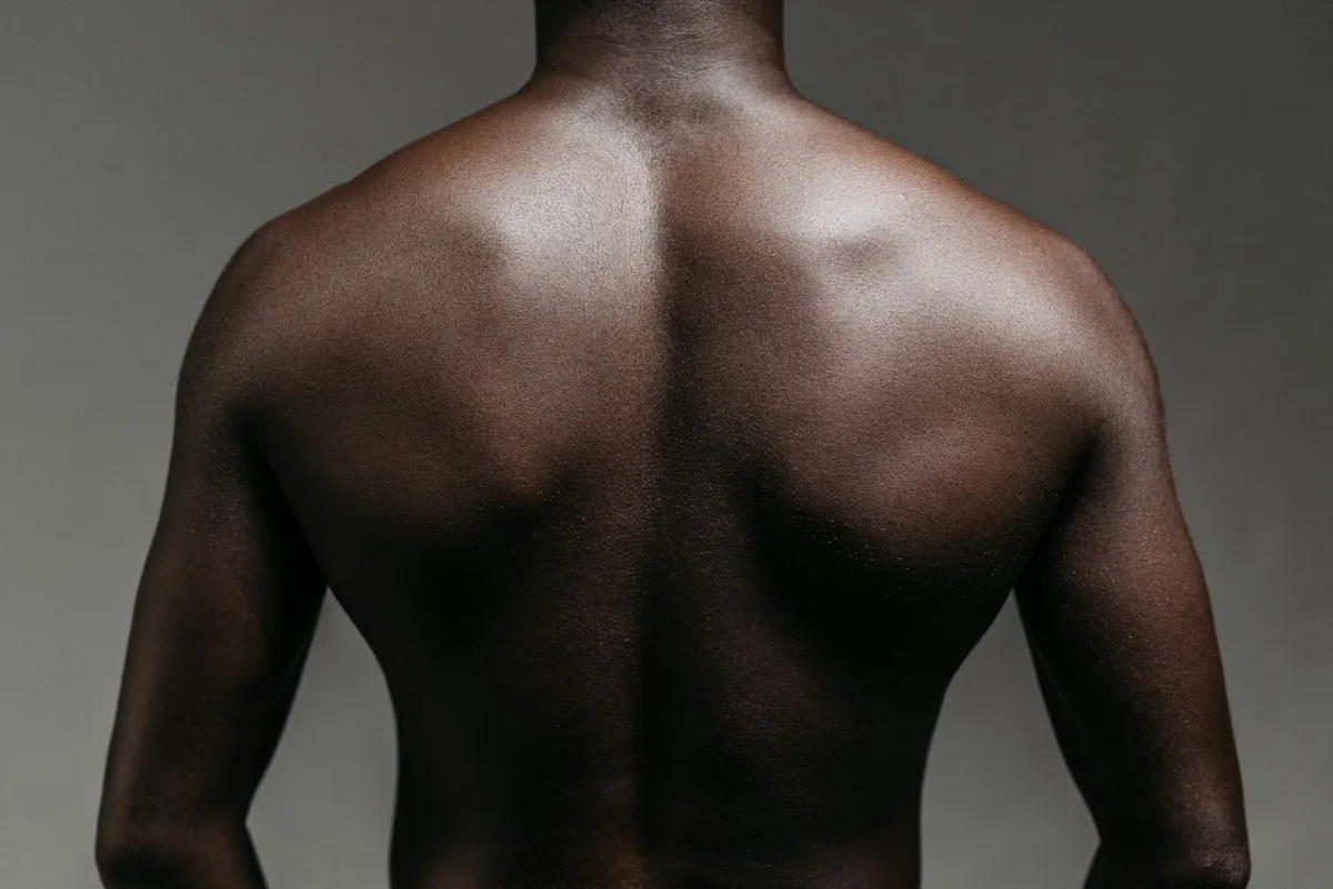 Close-up of a topless man's back in a studio shoot against a gray wall, showcasing strength and physique.