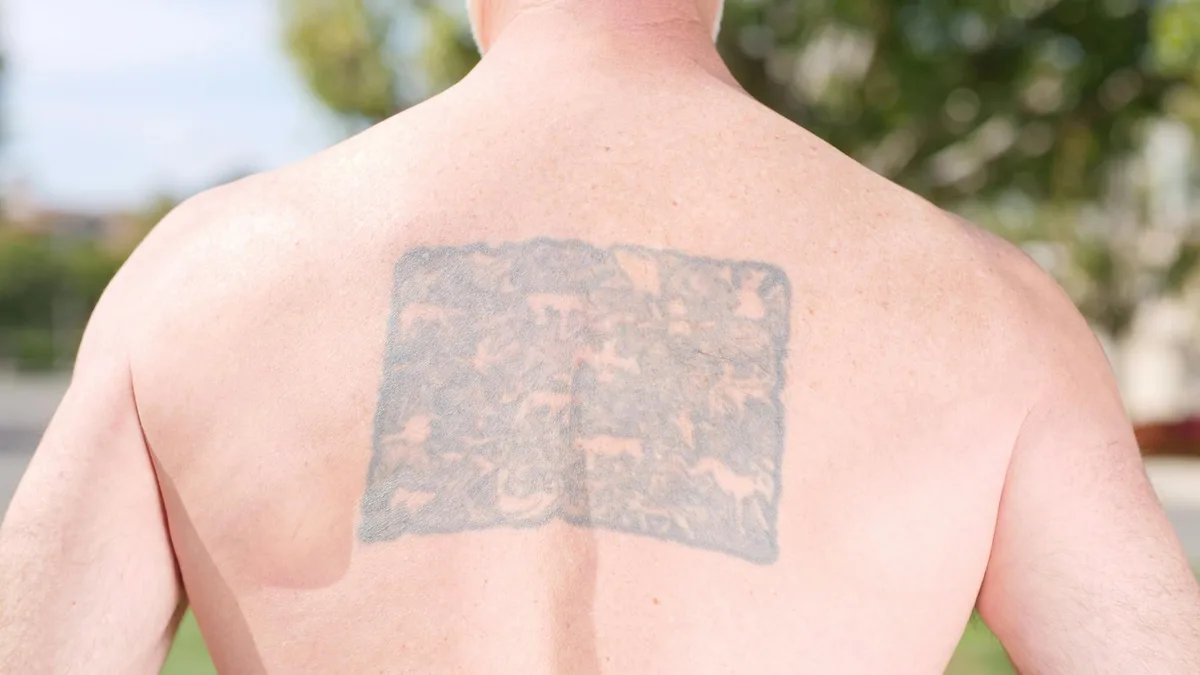 Close-up of a man's back with a tattoo in an outdoor setting.